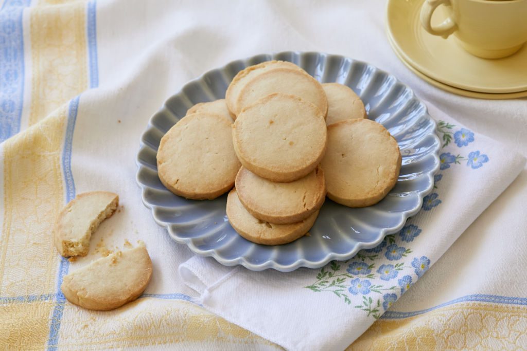 A pile of 3-ingredient shortbread cookies are served on a blue plate. One homemade shortbread cookie is snapped in half.