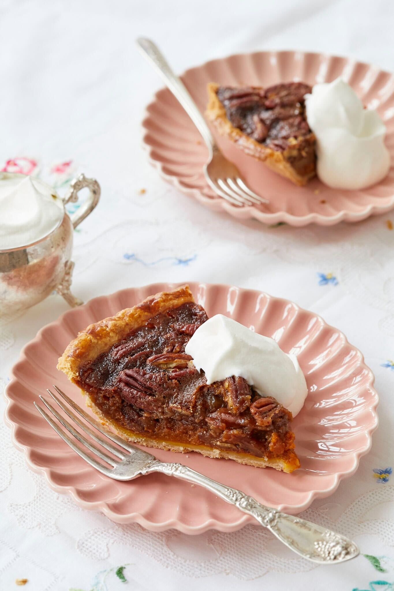 Two slices of Pumpkin Pecan Pies are served on two pink scallop-edged dessert plates with softly whipped cream. The pie has flaky crust, gooey filling, and crunchy caramelized pecans. 