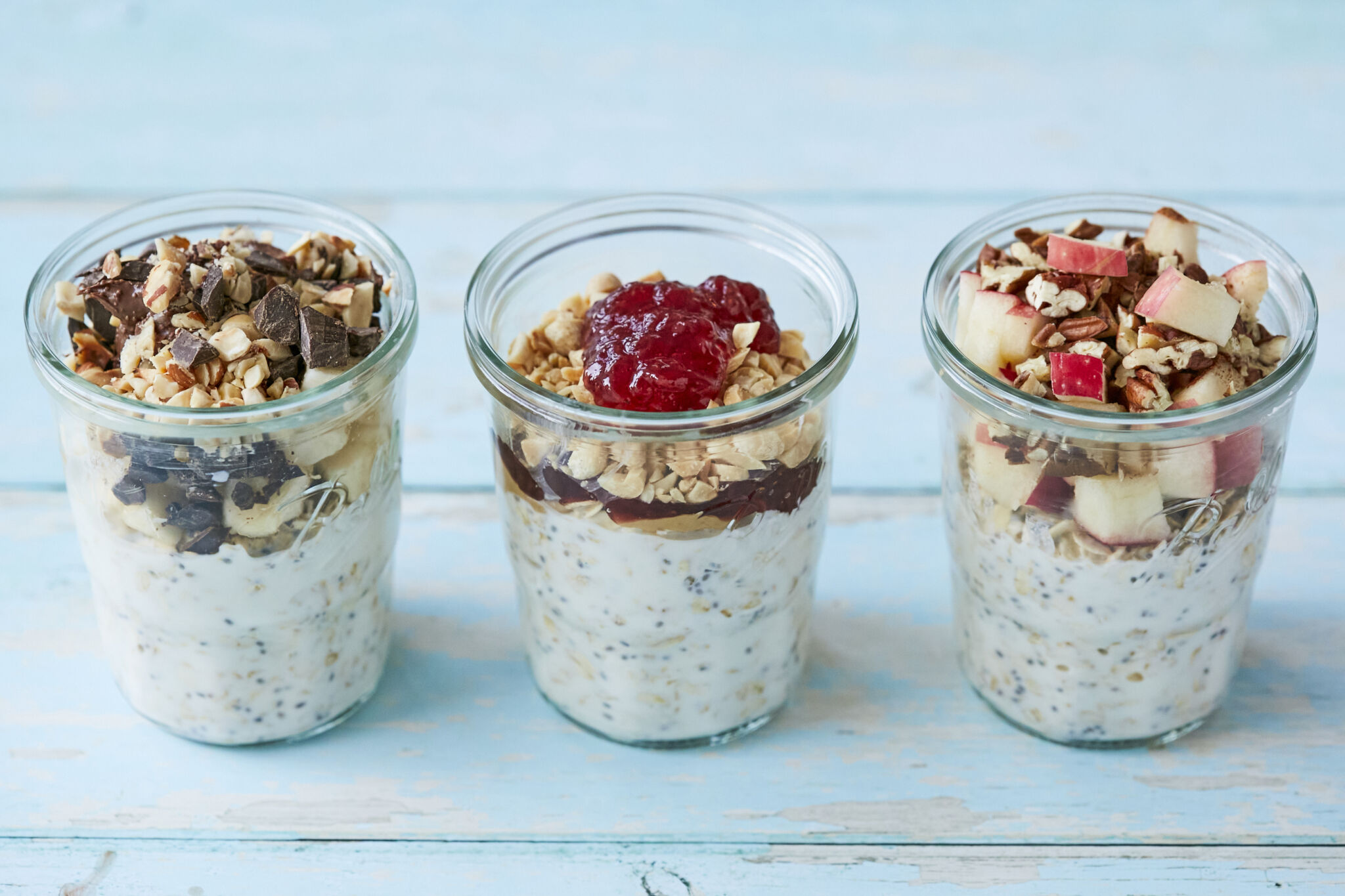 3 jars of Overnight Oats in banana Nutella, pb&j, and apple pie flavors, on a blue wooden table.