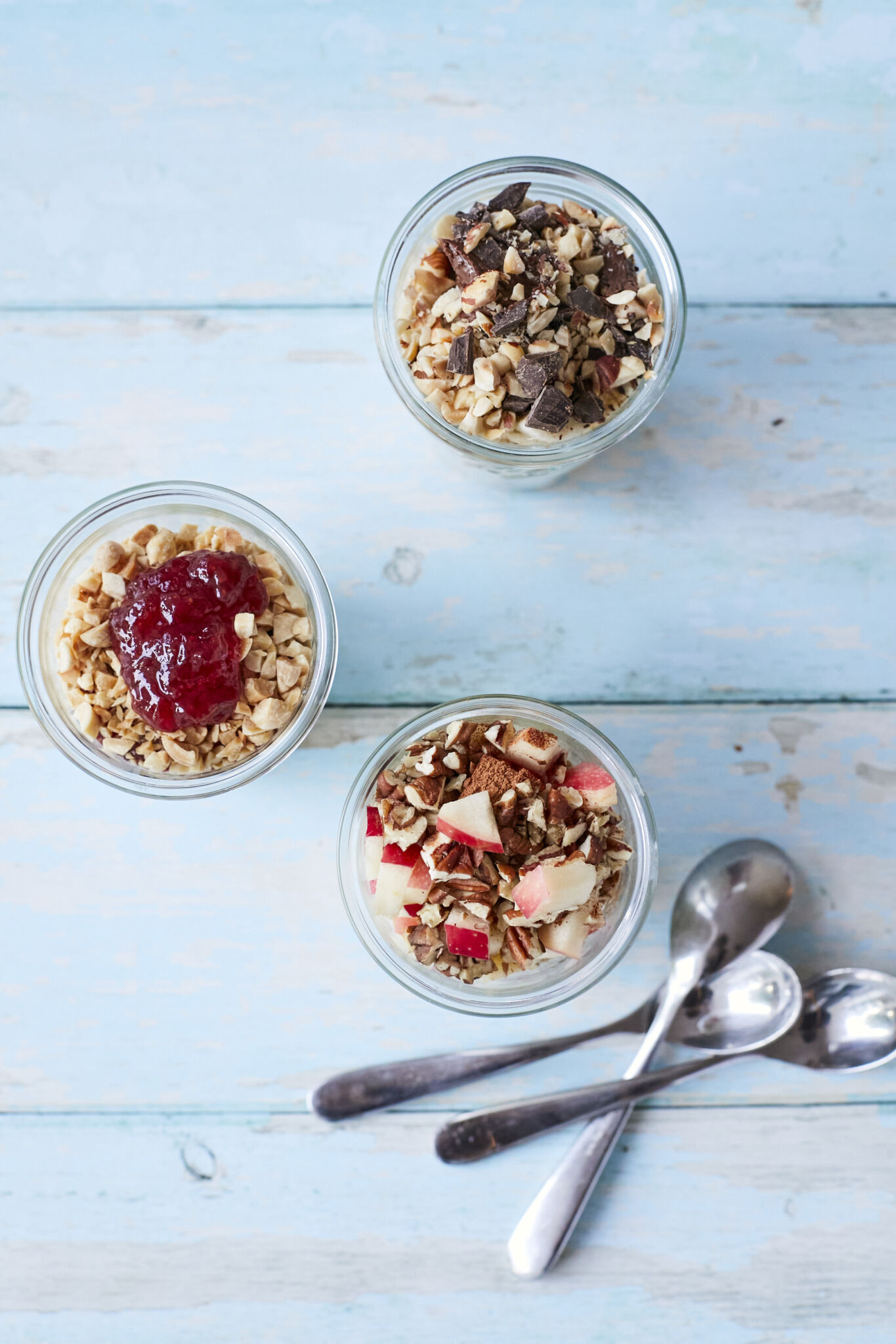 3 jars of Overnight Oats in 3 different flavors: banana Nutella, pb&j, and apple pie on a wooden table with metal spoons.